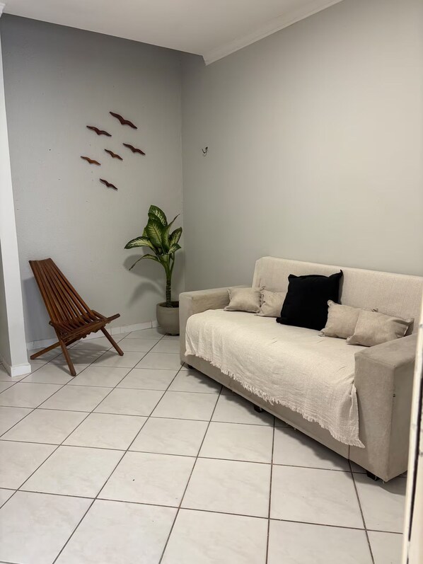 A living room with a beige sofa, a wooden chair, a potted plant, and wall art.