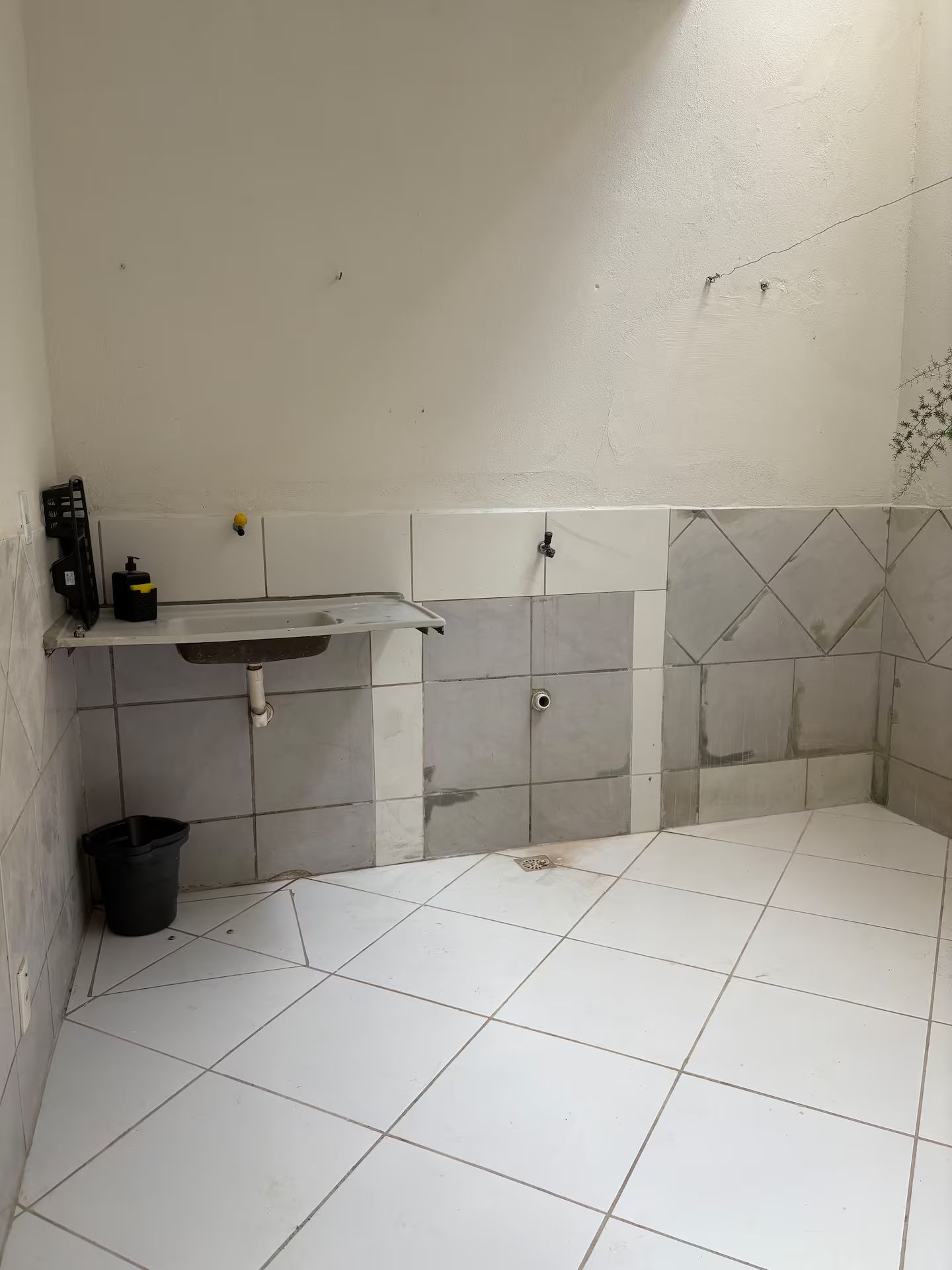 Une petite salle de bain avec un lavabo blanc, une poubelle noire et des murs carrelés.