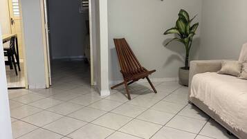Een kamer met een betegelde vloer, een houten stoel, een bank, een kamerplant en decoraties aan de muur.