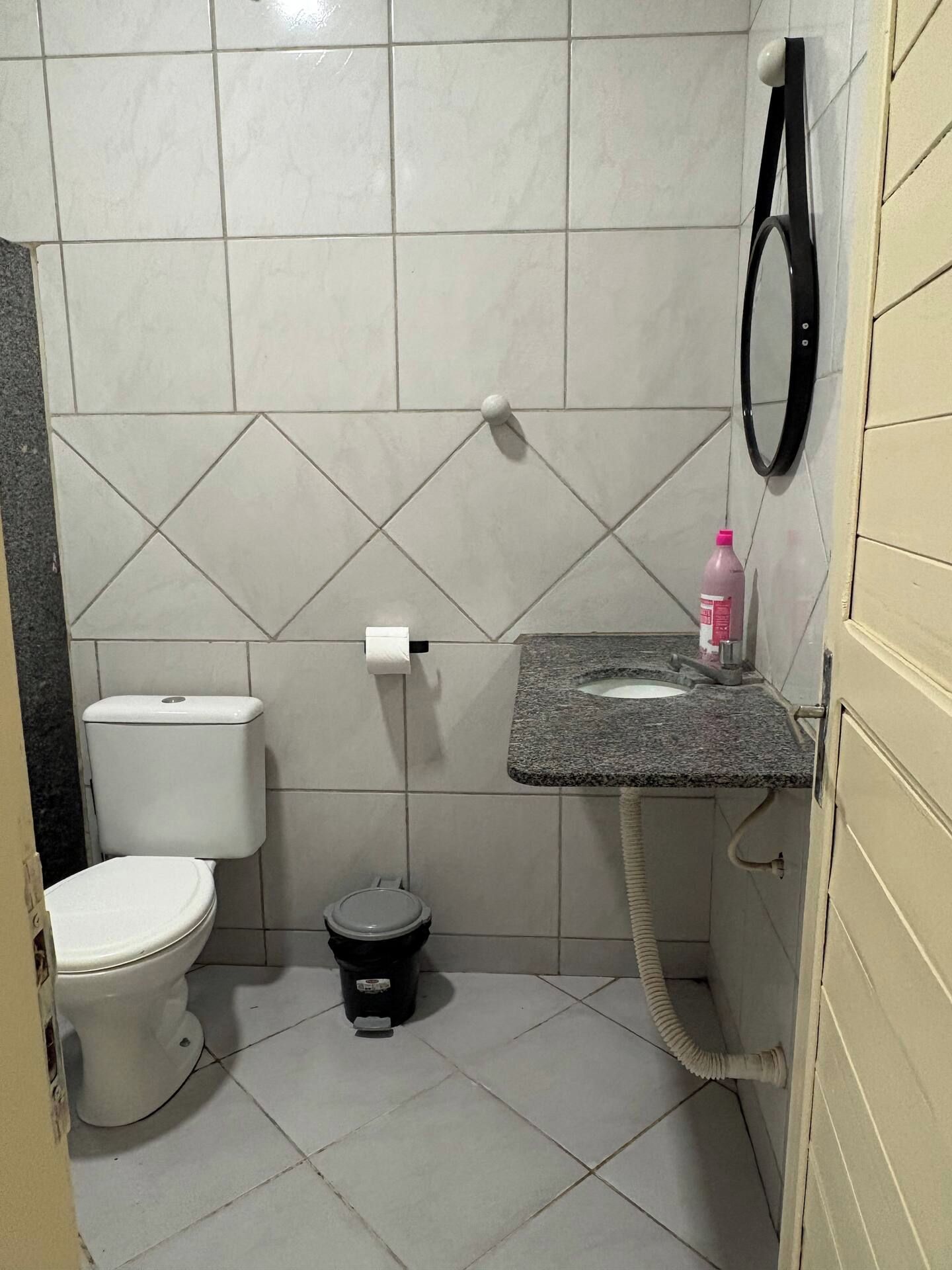 Casa de banho com sanita, um cesto de lixo, lavatório com dispensador de sabonete e barra de toalhas.