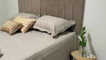 A bed with a headboard, pillows, and a bedside table with a plant and a device.