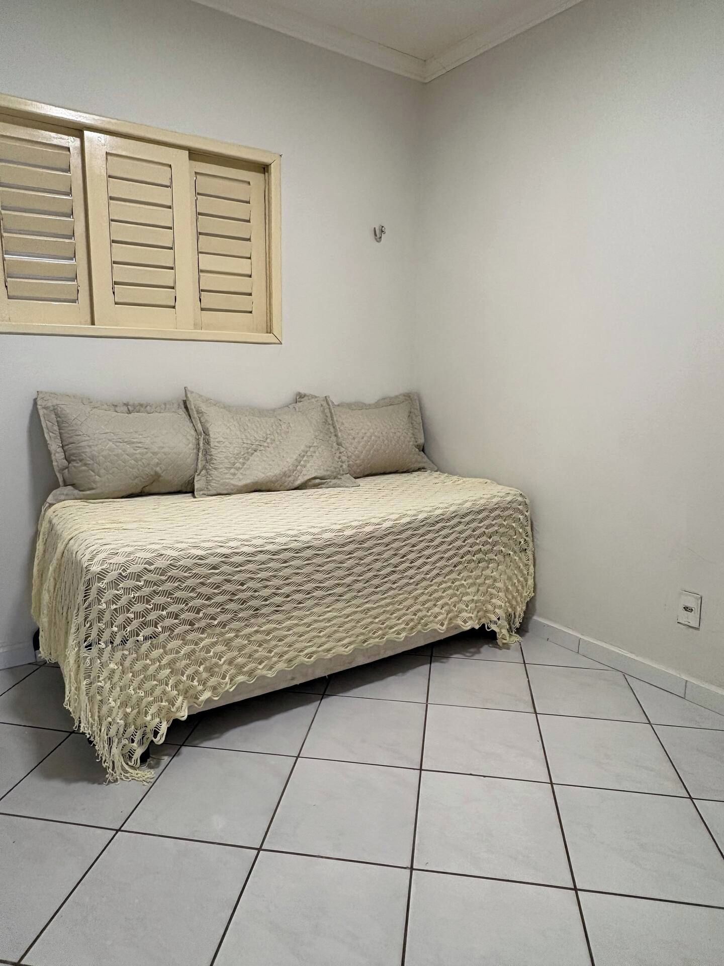 A bedroom with a bed, pillows, and a window with shutters.