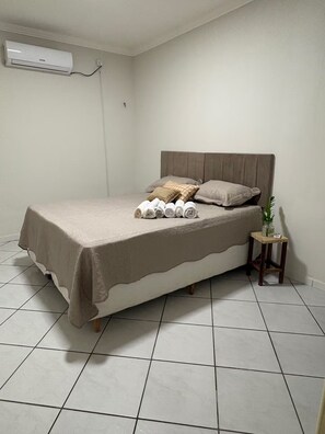 A bedroom with a bed, pillows, a bedside table with a plant, and an air conditioning unit on the wall. - Alameda House - 2 bedrooms and private garage (Mossoró)