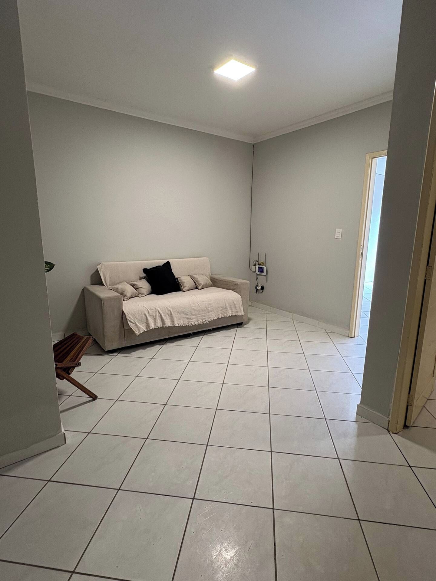 A spacious room with a large beige sofa, a tiled floor, and a ceiling light.