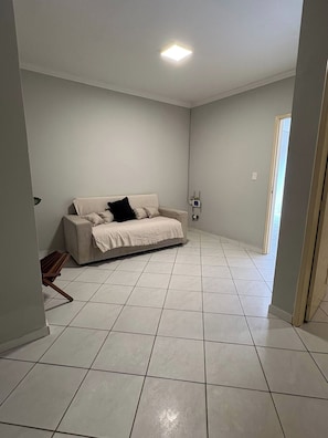 A spacious room with a large beige sofa, a tiled floor, and a ceiling light.