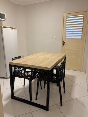A dining area with a wooden table and black chairs, a white refrigerator, and a door with horizontal blinds.