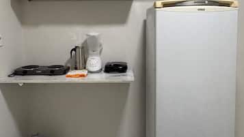 A compact kitchen with white cabinets, a built-in microwave, a coffee maker, and a refrigerator.