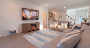 A living room with a fireplace, a large flat-screen TV, a sofa, and a dining area with chairs. - Pool | Jacuzzi | NO EXTRA FEE 5 min to beach (Palm Coast)