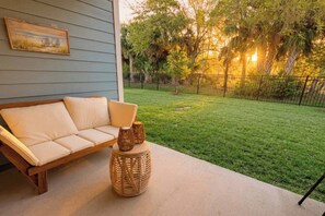A patio with a sofa and a wicker table, a grassy yard, and a fence. - Pool | Jacuzzi | NO EXTRA FEE 5 min to beach (Palm Coast)