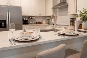 A modern kitchen with white cabinetry, stainless steel appliances, and a central island with a dining setup. - Pool | Jacuzzi | NO EXTRA FEE 5 min to beach (Palm Coast)