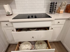 Uma cozinha com bancada branca, fogão preto e uma gaveta com panelas e utensílios.