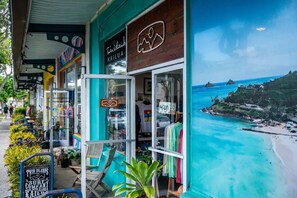 Ein Küstenladen mit Blick auf den Strand, Beschilderung für 'Twin Islands Surf Company' und Außenbereich mit Sitzgelegenheiten.