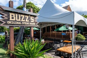 Ulkoterassi, jossa on pöytiä ja tuoleja, katettu ruokailutila sekä kyltti, jossa lukee: ”Buzz’s Original Steak House”.