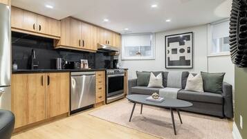 A compact living space with a kitchenette, a gray sofa with cushions, and a coffee table.