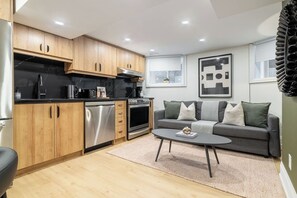 A compact living space with a kitchenette, a gray sofa with cushions, and a coffee table.