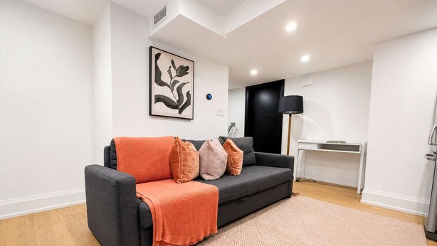 A modern living room with a grey sofa, orange throw, patterned rug, and a black floor lamp. - Stylish 2BR West End Oasis | Huge Deck near High Park (Toronto)