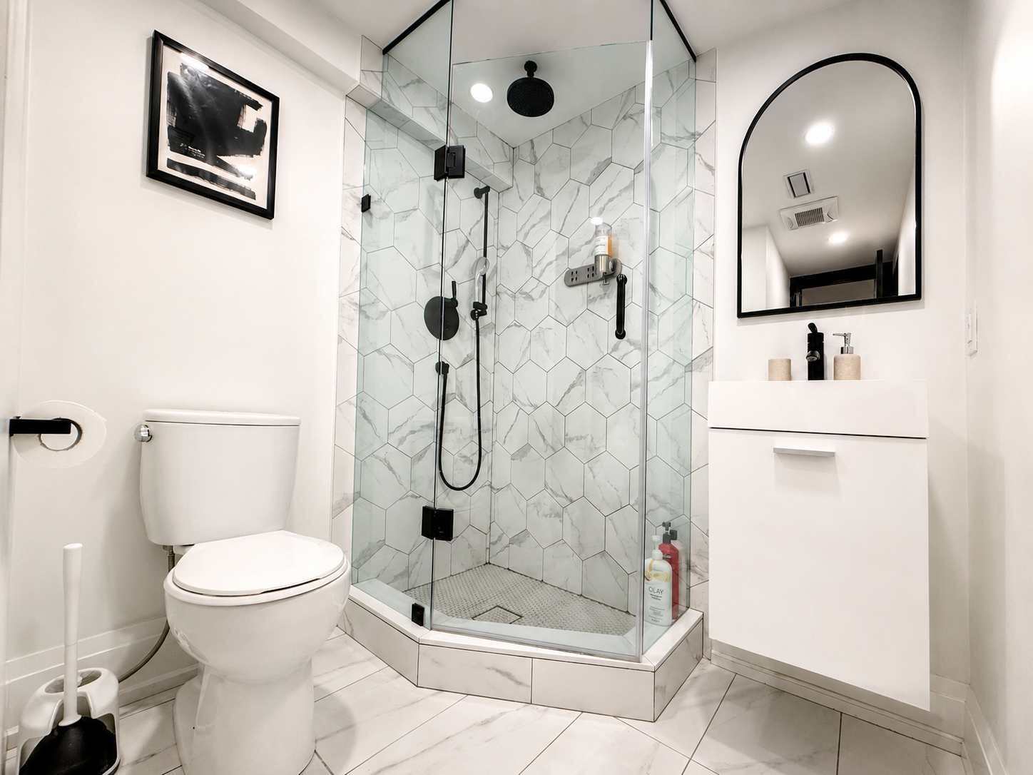 Un baño moderno con ducha envuelta en cristal, inodoro y tocador con espejo.