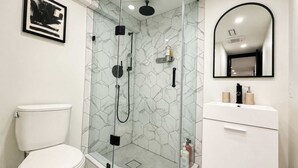 A modern bathroom with a glass-enclosed shower, a white toilet, and a vanity with a mirror. - Stylish 2BR West End Oasis | Huge Deck near High Park (Toronto)