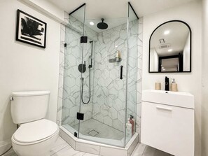 A modern bathroom with a glass-enclosed shower, a white toilet, and a vanity with a mirror. - Stylish 2BR West End Oasis | Huge Deck near High Park (Toronto)