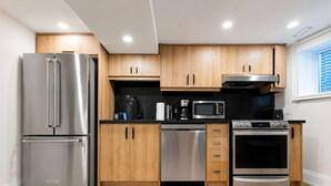 A modern kitchen with stainless steel appliances, wooden cabinets, and a black countertop. - Stylish 2BR West End Oasis | Huge Deck near High Park (Toronto)