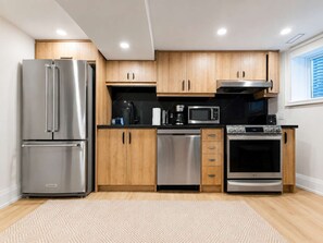 A modern kitchen with stainless steel appliances, wooden cabinets, and a black countertop. - Stylish 2BR West End Oasis | Huge Deck near High Park (Toronto)