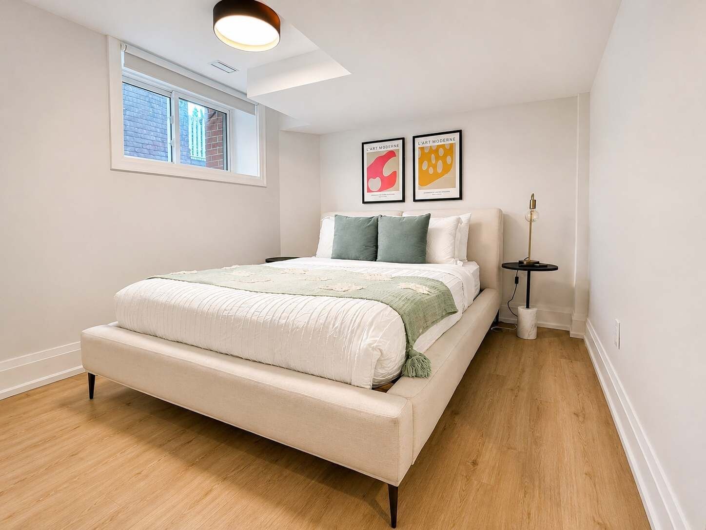 Un dormitorio con una cama, un ventanal, una lámpara de techo y dos cuadros en la pared.