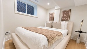 A bedroom with a bed, a window, a bedside table, and a lamp. - Stylish 2BR West End Oasis | Huge Deck near High Park (Toronto)
