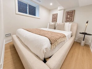 A bedroom with a bed, a window, a bedside table, and a lamp. - Stylish 2BR West End Oasis | Huge Deck near High Park (Toronto)