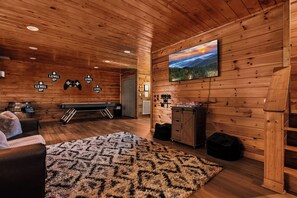 Ein gemütliches Blockhauss-Interieur mit Billardtisch, einem großen Teppich und einem Gemälde vom Sonnenuntergang.