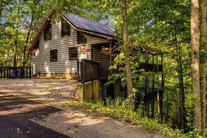 A log cabin with a metal roof, surrounded by trees and a gravel driveway. - Private King Suites, Hot Tub, Arcade, Private, Seasonal Mountain Views (Sevierville)