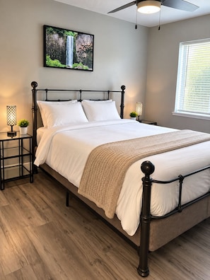 A neatly made bed with a headboard, two bedside tables with lamps, a wall-mounted TV, and a window with blinds. - Spacious 4-bedroom house in gorgeous Kennewick with AC (Kennewick)