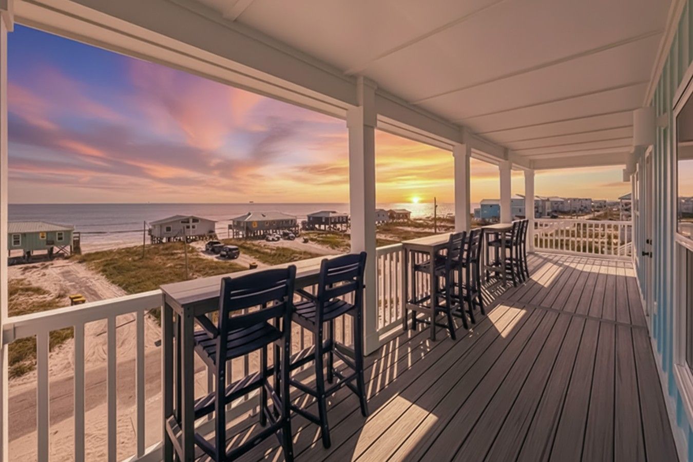 A wooden deck with chairs and a table, overlooking a beach with buildings in the distance.