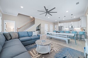 A modern living room with a sectional sofa, a round coffee table, and a dining area with a bench. - New Beginnings · New Lux Home*Private Pool*100ft to Beach*Elevator (Gulf Shores)