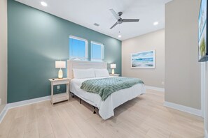 Ein Schlafzimmer mit einem Bett, Nachttischen, einem Deckenventilator und einem Fenster mit Jalousien.