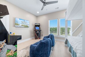 A room with a ceiling fan, a foosball table, a large window with blinds, and a bed with a white comforter. - New Beginnings · New Lux Home*Private Pool*100ft to Beach*Elevator (Gulf Shores)