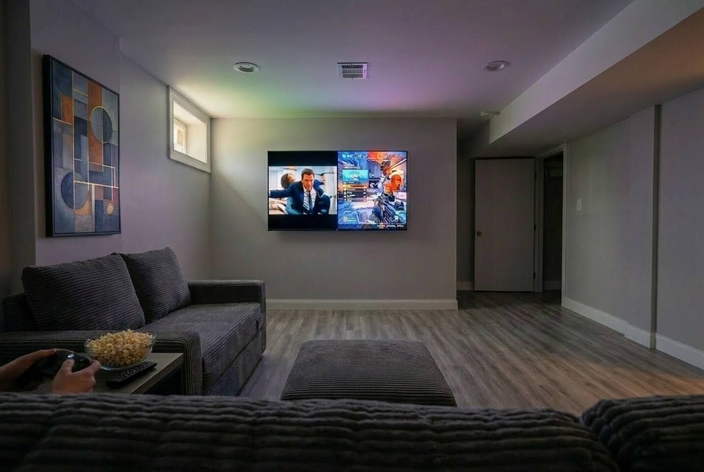 Una sala de estar moderna con un televisor de pantalla plana montado en la pared, un sofá de color oscuro y suelo de madera.