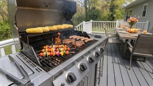 A Char-Broil grill with corn, sausages, and skewers on a deck. - Riverfront Front | Fire Pit | Arcade | Fishing| (New Brunswick)