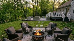 A patio with outdoor furniture, a fire pit, and a house with a deck in the background. - Riverfront Front | Fire Pit | Arcade | Fishing| (New Brunswick)