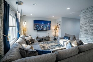 Una sala de estar moderna con un amplio sofá, un televisor de pantalla plana y un cuadro de un paisaje urbano.