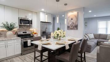 Una cocina moderna con armarios blancos, electrodomésticos de acero inoxidable y una zona de comedor con una mesa vestida para cuatro.