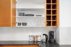 A kitchen with open wooden cabinets, a countertop with a coffee maker, and storage jars. - Modern Yonge-Dundas Studio | Steps to Eaton Centre | Parking Available (Toronto)