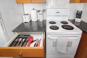 Eine Küche mit einem Herd, einer Schublade voller Küchenutensilien und einer Arbeitsplatte mit Toaster und Papierhandtuchhalter.