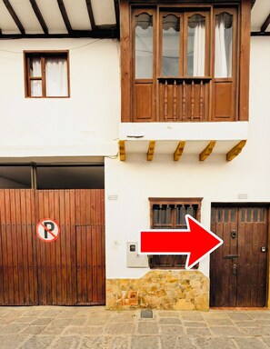 A two-story building with a wooden balcony, a garage door, and a no parking sign.