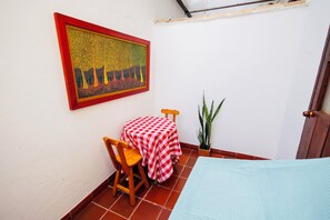 Une petite pièce avec une table à carreaux, une chaise, une plante en pot et un tableau accroché au mur.