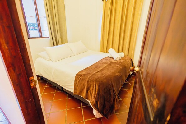 A hotel room with a bed, curtains, and a tiled floor.