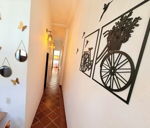 A hallway with decorative wall art including a bicycle and a basket, and a tiled floor.