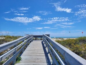 Ein hölzerner Steg führt zu einem Strand unter blauem Himmel.