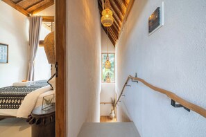 Un couloir étroit avec un lit, un luminaire suspendu et un porte-objets fixé au mur.