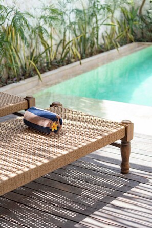 Ein Korbsessel mit Handtuch und Blume, platziert auf einer Holzterrasse an einem Pool.