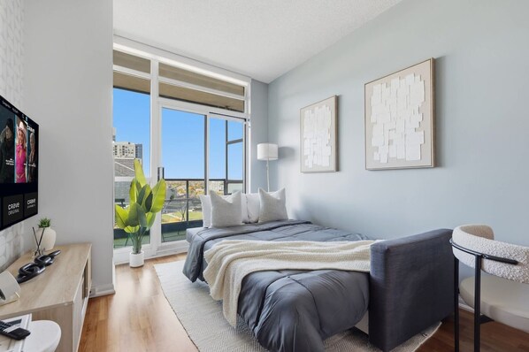 A modern bedroom with a bed, a desk, a chair, and a television.